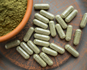 Supplement kratom green capsules and powder on brown plate. Herbal product alt-medicine kratom is opioid. Home alternative pain remedy, opioid addiction, dangerous painkiller, overdose. Close up. Selective focus