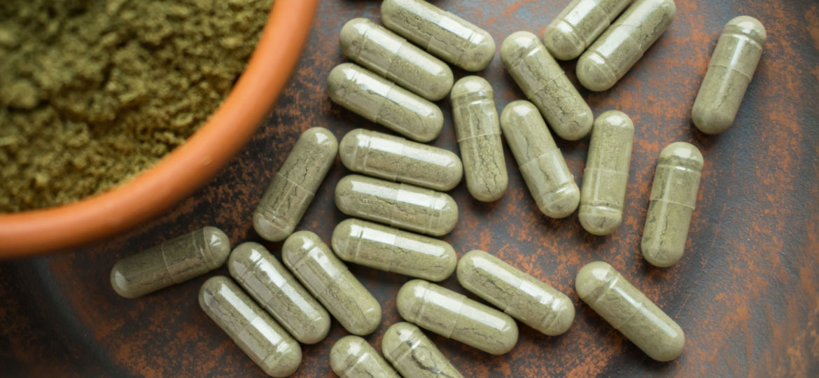 Supplement kratom green capsules and powder on brown plate. Herb