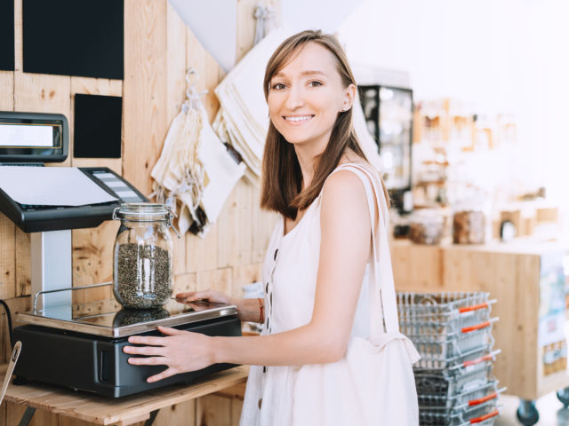 Girl weighs glass jar with hemp seeds in zero waste shop